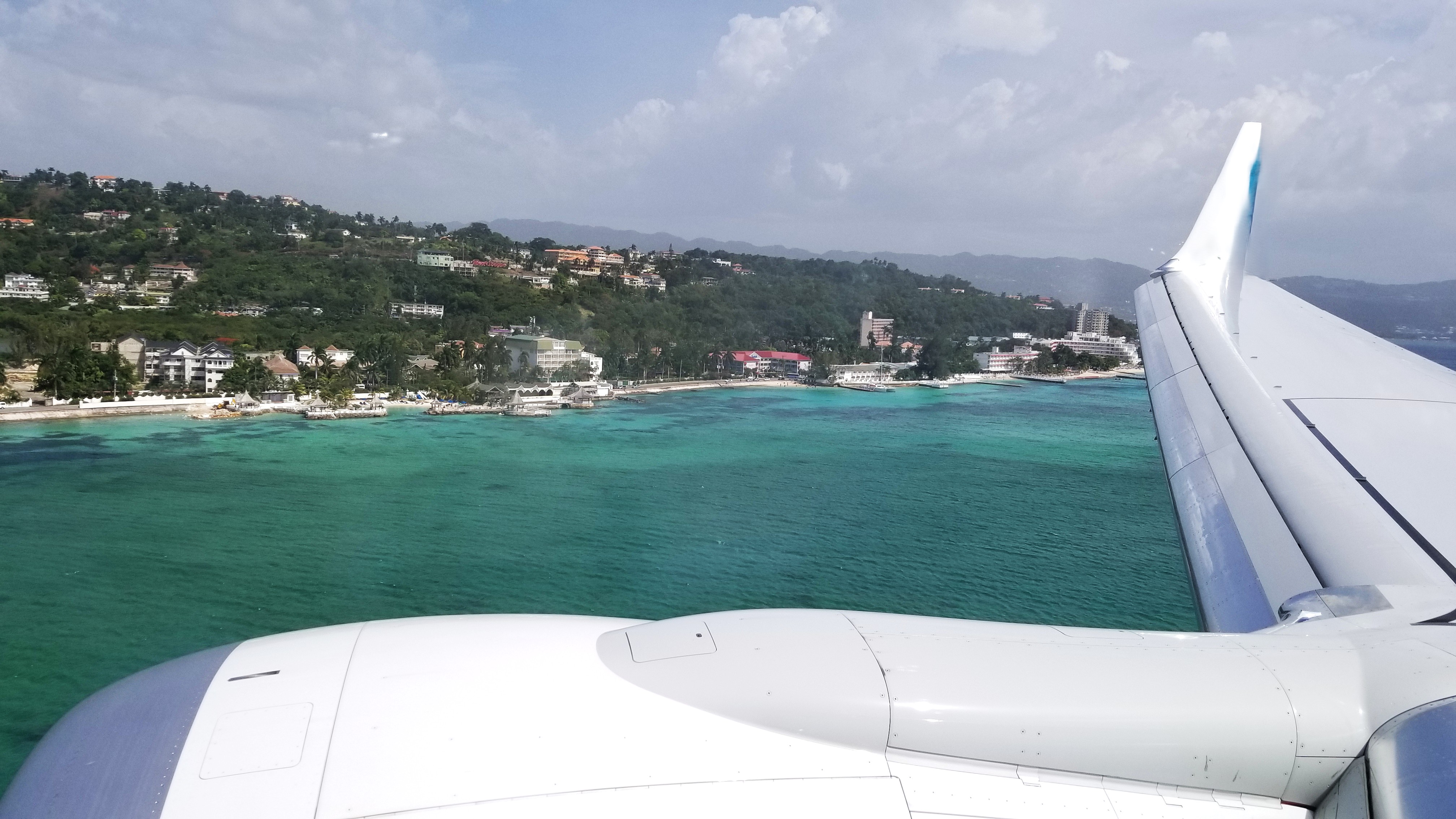 View from a plane window on approach to Jamaica, turquoise north coast water and resorts below the wing