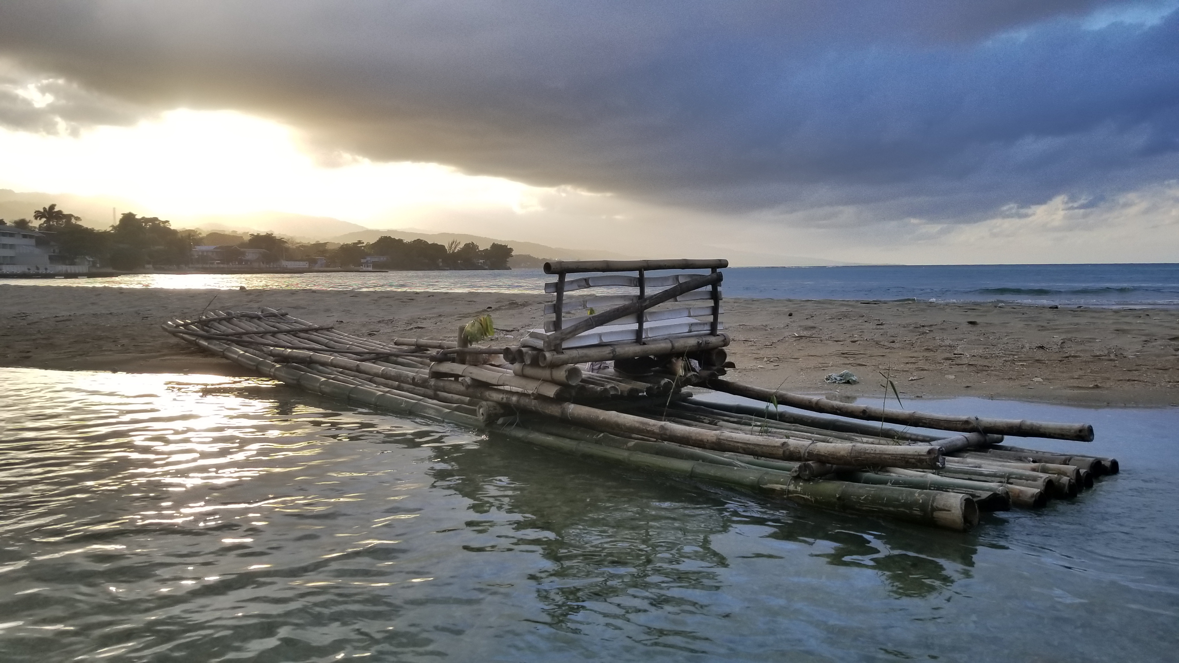A bamboo raft resting at the water's edge in Jamaica at sunset